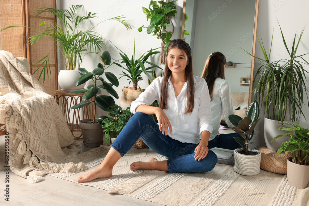 Happy young woman sitting near mirror and different houseplants in room Happy young woman sitting near mirror and different houseplants in room