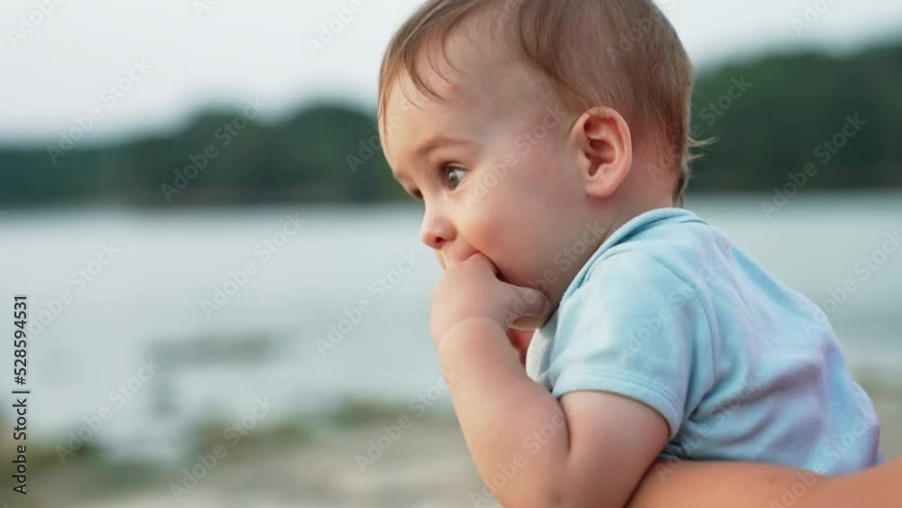 Little baby boy with fingers in his mouth. Mother holding a cute child in hands in nature. Close up. Blurred backdrop. Little baby boy with fingers in his mouth. Mother holding a cute child in hands in nature. Close up. Blurred backdrop.