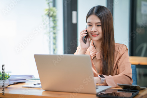 Asian businesswoman talking on mobile phone in front of a laptop computer at office