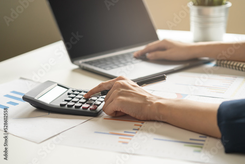 Account finance, asian young business woman hand use calculator for calculate budget, cost and income of company from charts, reports paperwork, plan spend money expenses, working on desk at home.