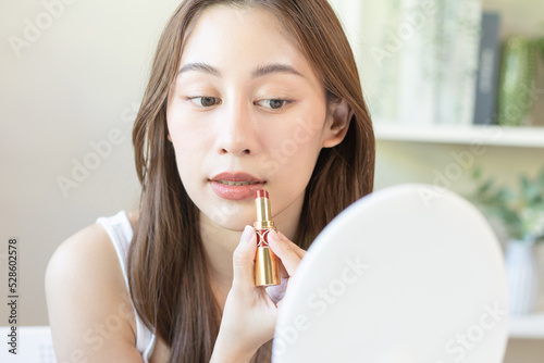 Skin care cosmetics concept  hand of woman  girl make up face by applying red lipstick  lips balm on her mouth  looking at the mirror at home. Female look with natural fashion style.