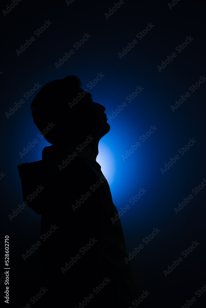 Cleanly define silhouette of man looking up wearing hood blue background