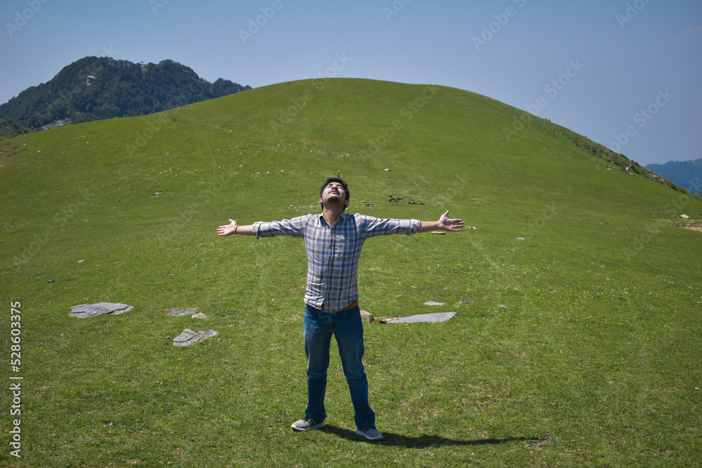 Fototapeta premium Happy guy in high altitude green grassland during day time arms outstretched