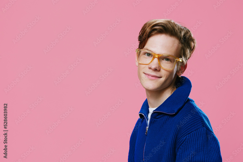 close-up portrait of a nice, pleasantly smiling guy in a blue zip-up jacket, glasses with transparent lenses and orange frames. Pink background with space for text close-up portrait of a nice, pleasantly smiling guy in a blue zip-up jacket, glasses with transparent lenses and orange frames. Pink background with space for text