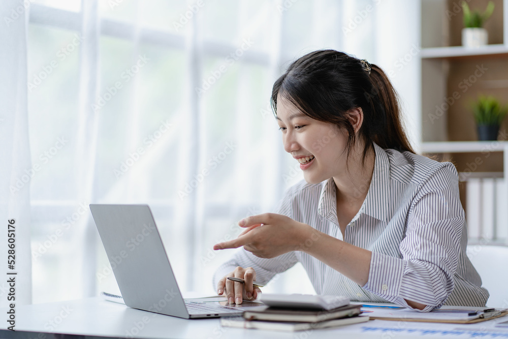 Asian woman working at home on desk using calculator to calculate tax accounting expense report with graph document and laptop computer. Asian woman working at home on desk using calculator to calculate tax accounting expense report with graph document and laptop computer.