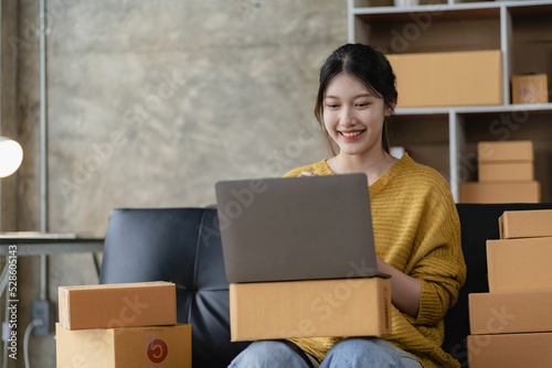 Asian woman working at home with yellow box and laptop for taking orders, sme business ideas on parcel delivery © ArLawKa