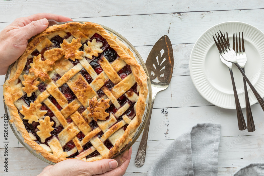 Hands holding a fresh cherry pie with serving plates to the side. Hands holding a fresh cherry pie with serving plates to the side.