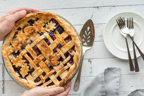 Hands holding a fresh cherry pie with serving plates to the side.