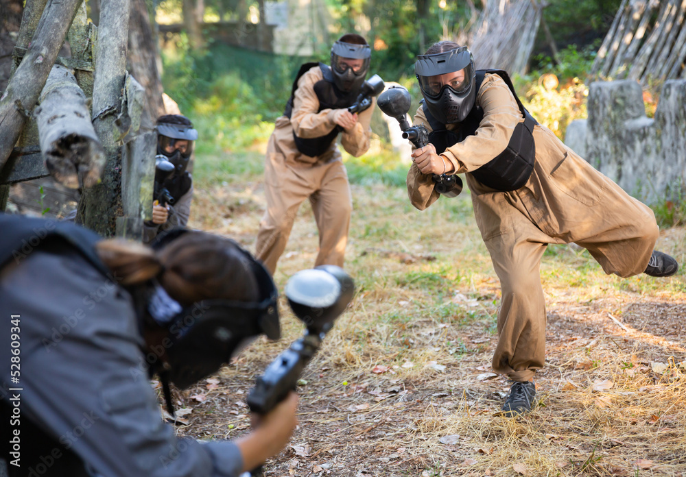 Fototapeta premium Team eliminating opponents on paintball field. People in protective outwear and helmets aiming with paintball markers.