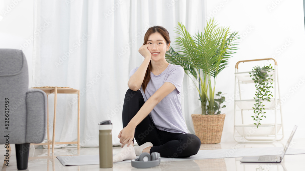 Beautiful Asian woman in sportswear is warming up or doing light exercises in the house with dumbbells and a protein shake or bottle of water and using a laptop at home, Healthy exercise. Beautiful Asian woman in sportswear is warming up or doing light exercises in the house with dumbbells and a protein shake or bottle of water and using a laptop at home, Healthy exercise.