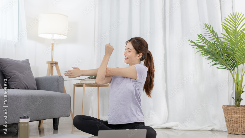 Beautiful Asian woman in sportswear is warming up or doing light exercises in the house with dumbbells and a protein shake or bottle of water and using a laptop at home, Healthy exercise. Beautiful Asian woman in sportswear is warming up or doing light exercises in the house with dumbbells and a protein shake or bottle of water and using a laptop at home, Healthy exercise.