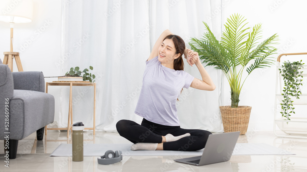 Beautiful Asian woman in sportswear is warming up or doing light exercises in the house with dumbbells and a protein shake or bottle of water and using a laptop at home, Healthy exercise. Beautiful Asian woman in sportswear is warming up or doing light exercises in the house with dumbbells and a protein shake or bottle of water and using a laptop at home, Healthy exercise.
