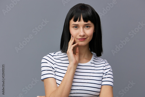 a sweet, attractive woman stands on a gray background in a white striped T-shirt and smiling pleasantly holds her fingers near her face in a relaxed gesture. Horizontal photo