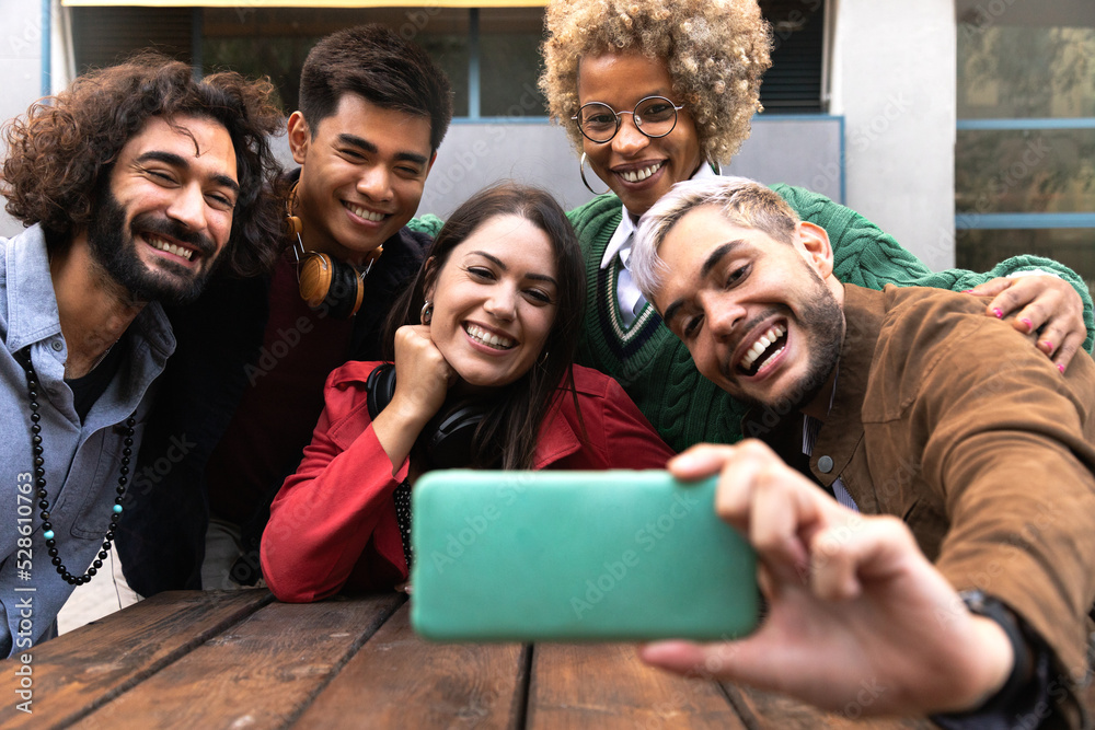 Obraz premium Smiling multiracial young friends take selfie together with mobile phone outdoors