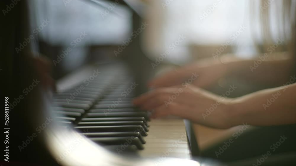 Close-up tracking shot of unrecognizable talented young woman pianist playing gentle music on beautiful grand piano sitting on background of window, slow motion, selective focus in rays of sun.