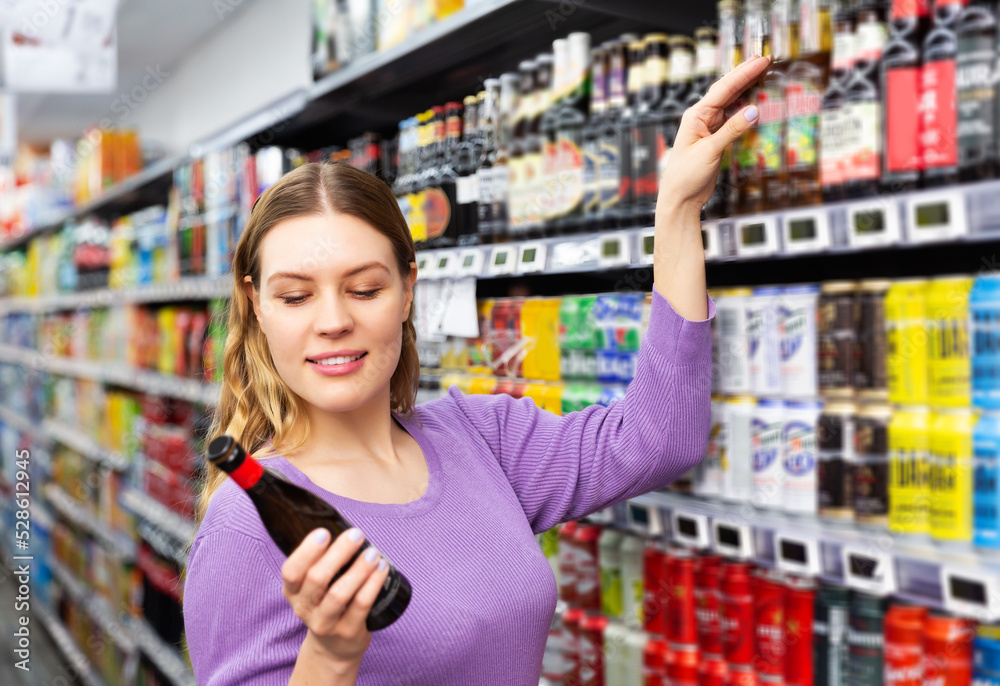 Portrait of happy young woman customer buying bottle of beer in the supermarket
