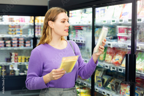 Young glad positive smiling woman choosing sliced cheese at food department in supermarket