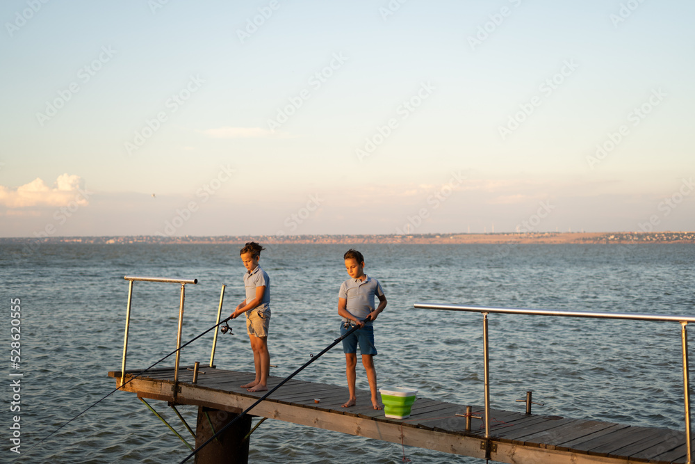 Little boys is fishing at sunset on the lake. Summer hobby and leisure