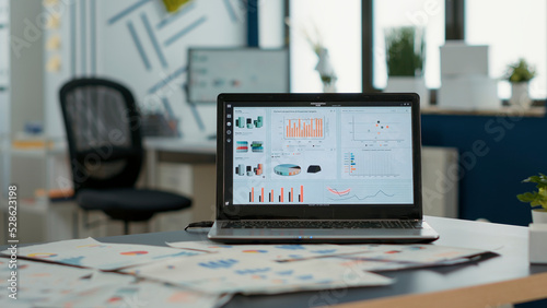 Closeup of laptop screen with enterprise resource planning showing moving charts and growing turnover in empty startup office. Interior of sales department with portable computer with erp software.