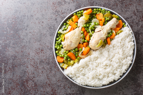 Chicken drumsticks stewed with carrots and green peas, served with rice close-up in a plate on the table. Horizontal top view from above photo