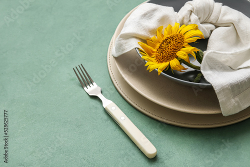 Dinnerware and sunflower in plate on green table