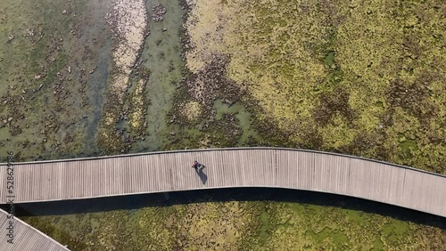 Man walking on a long wooden old bridge over a dried beach in the mediterranean photo