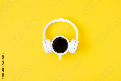 A cup of black coffee and white headphones on yellow background. Minimal style, Flat lay, Top view. Education concept