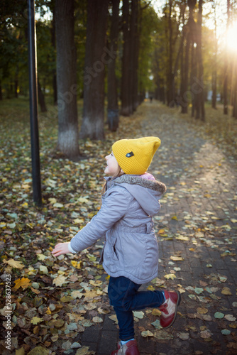 funny portrait of person child in demi-season clothes jacket and hat against background of autumn park and trees