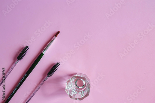 Fototapeta Naklejka Na Ścianę i Meble -  Materials for depilation of eyebrows on a pink background. Wooden stick for wax, brushes, brush for coloring, tweezers