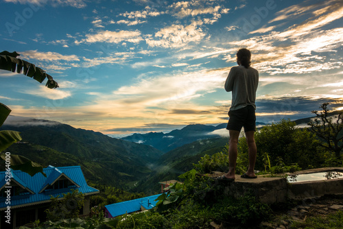 July 22nd 2021. Uttarakhand India. A man standing on a hill top looking at the landscape during sun set with beautiful multicolor cloudscape in the hills of the himalayas.