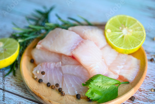fish fillet on wooden plate with ingredients for cooking, fresh raw pangasius fish fillet with herb and spices black pepper lemon lime and rosemary, meat dolly fish tilapia striped catfish