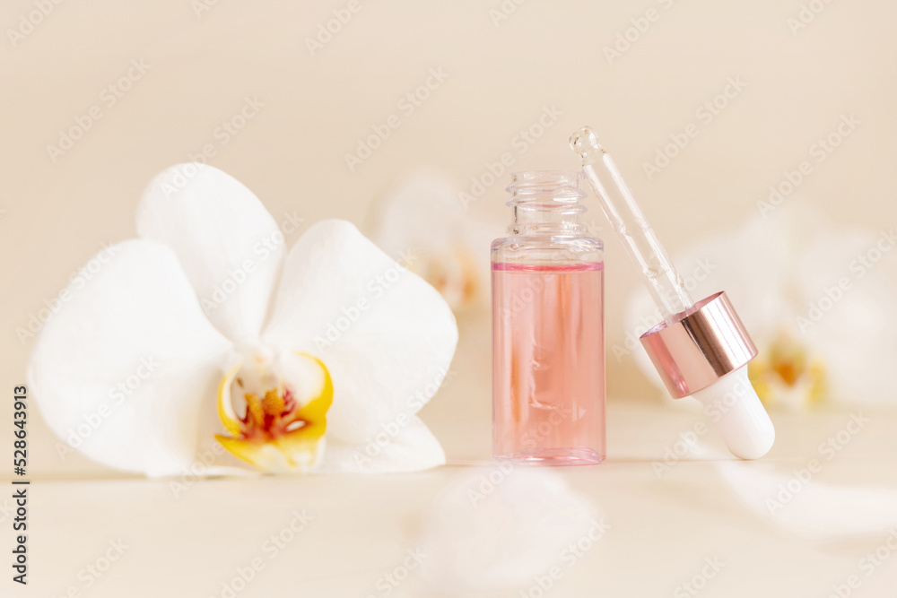 Opened Dropper Bottle near white orchid flowers on light beige close up. Skincare beauty product