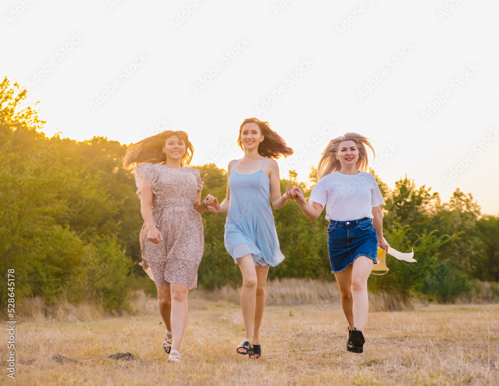 Fototapeta premium A group of girlfriends jumps and runs outdoors. A group of female friends hugs and enjoys the sunset in nature. Laughter, smiles and joy.