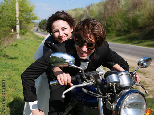 Unusial wedding on the motocycle. the bride in a leather jacket, the groom in glasses. Happy couple smiling outdoors