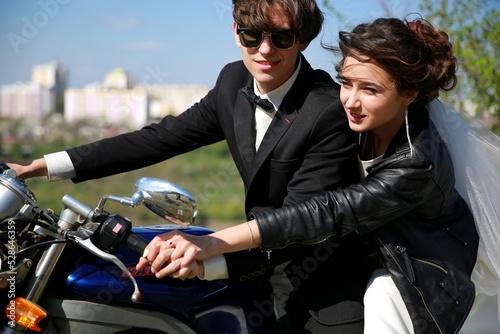 Unusial wedding on the motocycle. the bride in a leather jacket, the groom in glasses. Happy couple smiling outdoors photo
