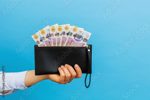 Female hands holding british pounds banknotes in black wallet on a blue background. photo