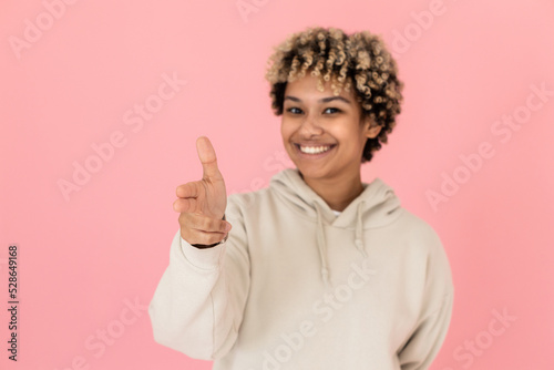 Blurry African American imitating shooting in studio. Female model with curly hair pointing finger gun at camera. Portrait, studio shot, fun concept