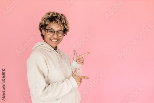 Portrait of optimistic African American woman. Female model in hoodie and glasses smiling and pointing copy space. Portrait, emotion concept