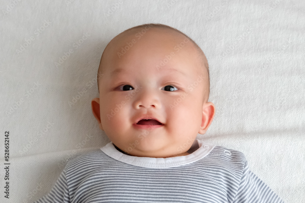 A baby in a striped shirt lies smiling on the white carpet.