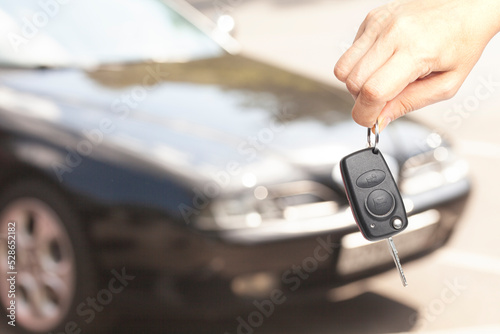 Car key in woman's hand with a car blurred in the background © yurchello108
