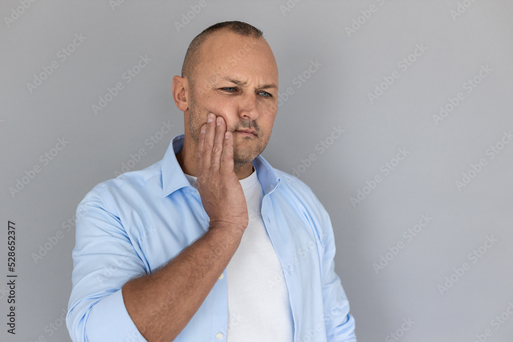 Portrait of mature Caucasian man suffering from toothache. Balding guy wearing white T-shirt and blue shirt touching his cheek. Toothache concept Portrait of mature Caucasian man suffering from toothache. Balding guy wearing white T-shirt and blue shirt touching his cheek. Toothache concept