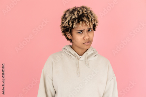 Frowning African American woman in studio. Female model with curly hair looking at camera with frown. Portrait, emotion, studio shot concept