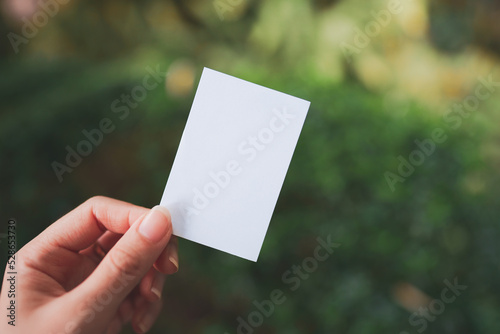 Woman's hand holding a small blank white paper with blurred nature background.