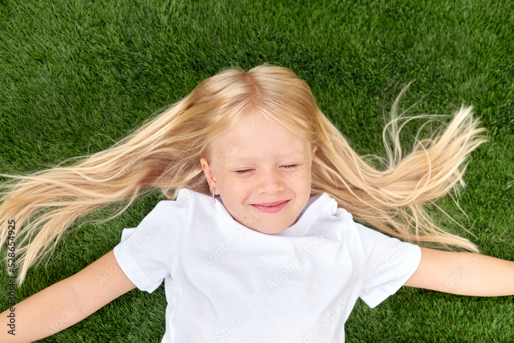Pretty blonde girl with closed eyes lying on green grass. Mock up white t shirt. Top view. Pretty blonde girl with closed eyes lying on green grass. Mock up white t shirt. Top view.
