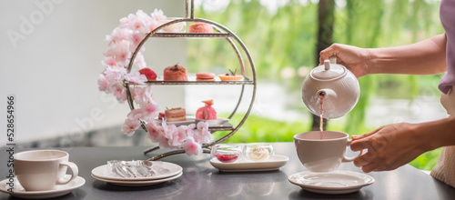 Panel kuchenny z motywem Woman hand pouring hot tea with Afternoon tea set and Pink dessert at luxury hotel