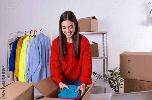 Young woman, owener of small business packing product in boxes, preparing it for delivery. Women packing package with her products that she selling online photo