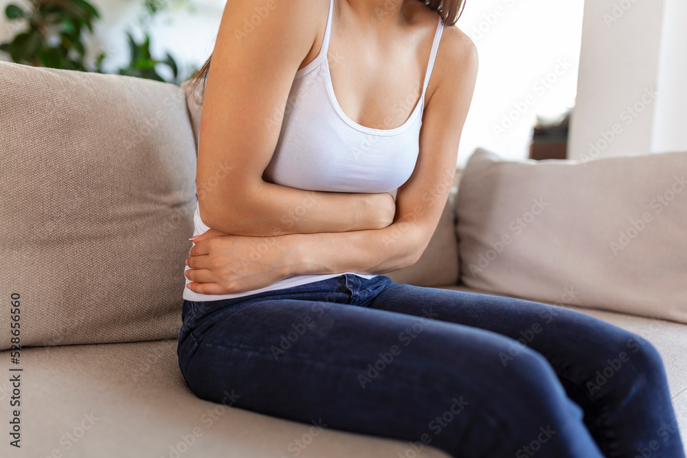 Woman in painful expression holding hands against belly suffering menstrual period pain, lying sad on home bed, having tummy cramp in female health concept Woman in painful expression holding hands against belly suffering menstrual period pain, lying sad on home bed, having tummy cramp in female health concept
