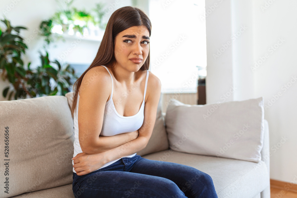Woman in painful expression holding hands against belly suffering menstrual period pain, lying sad on home bed, having tummy cramp in female health concept Woman in painful expression holding hands against belly suffering menstrual period pain, lying sad on home bed, having tummy cramp in female health concept