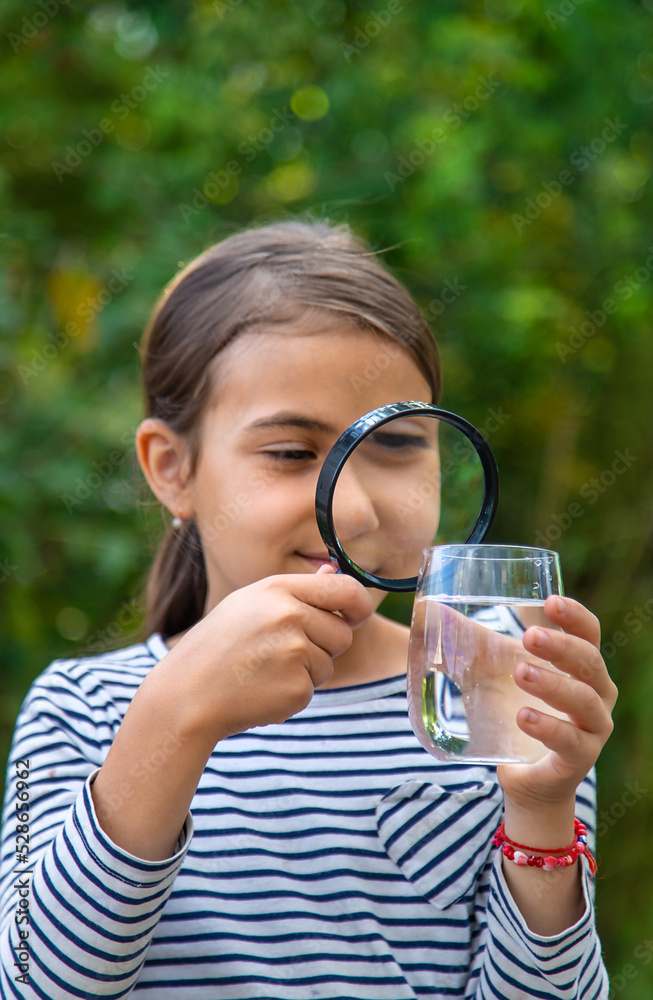 The child examines the water with a magnifying glass. Selective focus. The child examines the water with a magnifying glass. Selective focus.
