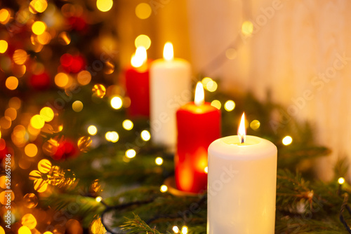 Close up shot of burning candles with blurred Christmas light and fir tree branches background. Warm  cozy atmosphere indoor